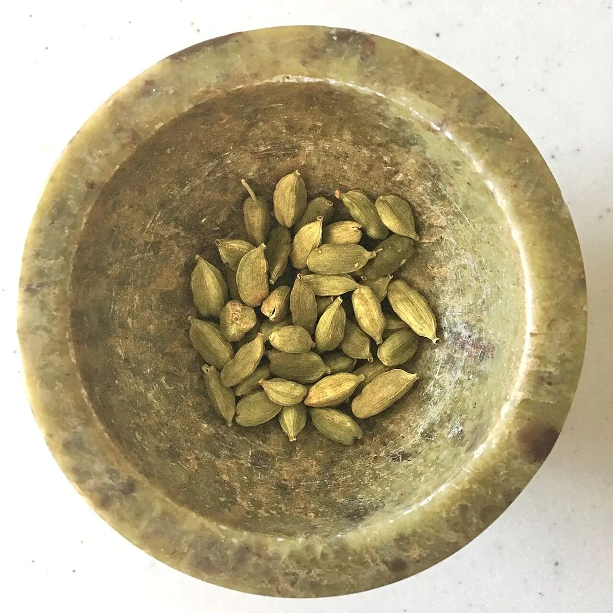 Green cardamom pods in a small brass bowl.