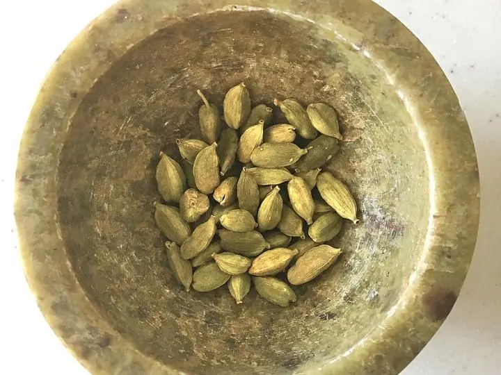 Green cardamom pods in a small brass bowl.